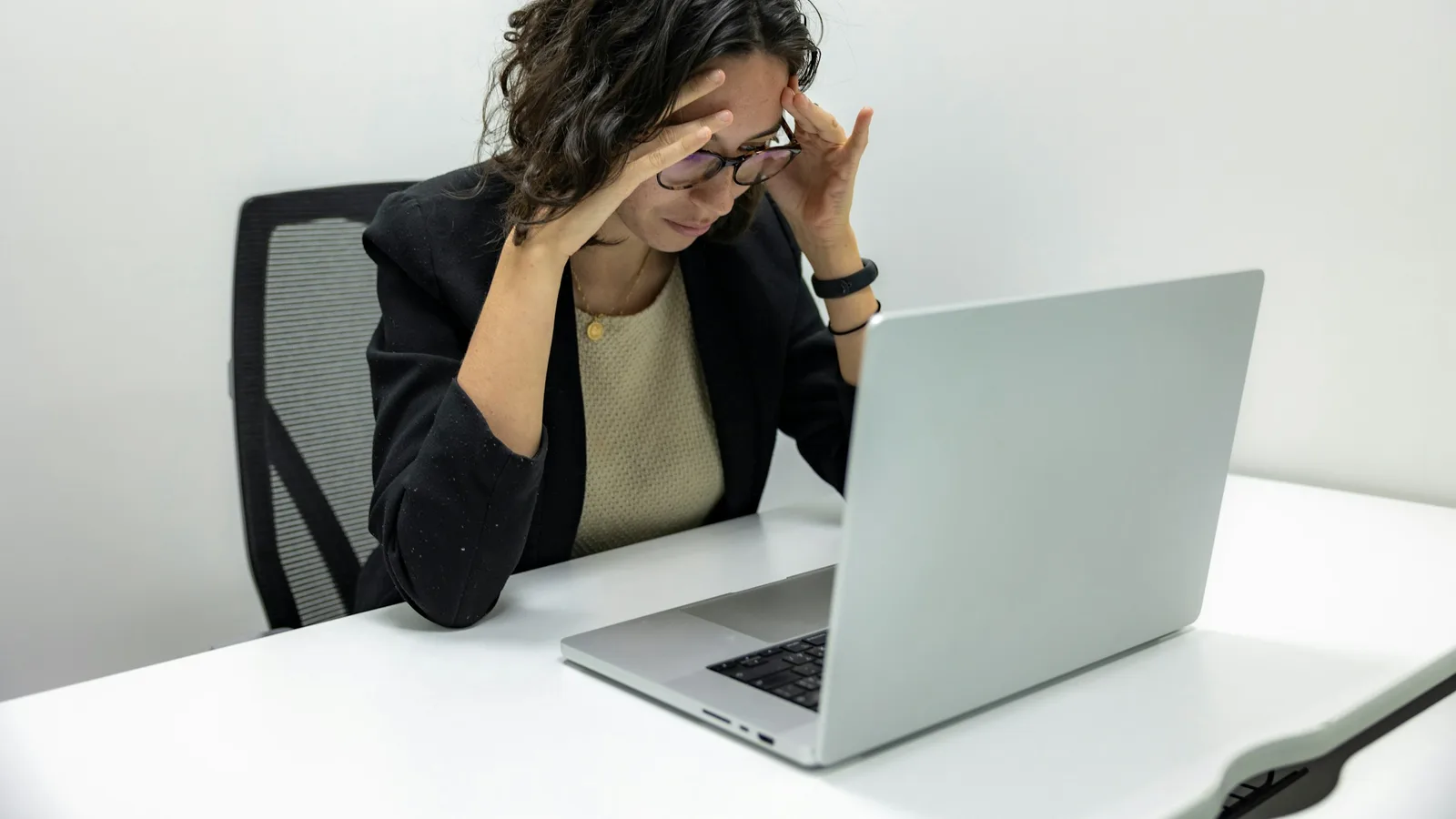 A woman rubbing her temples in frustration at a laptop