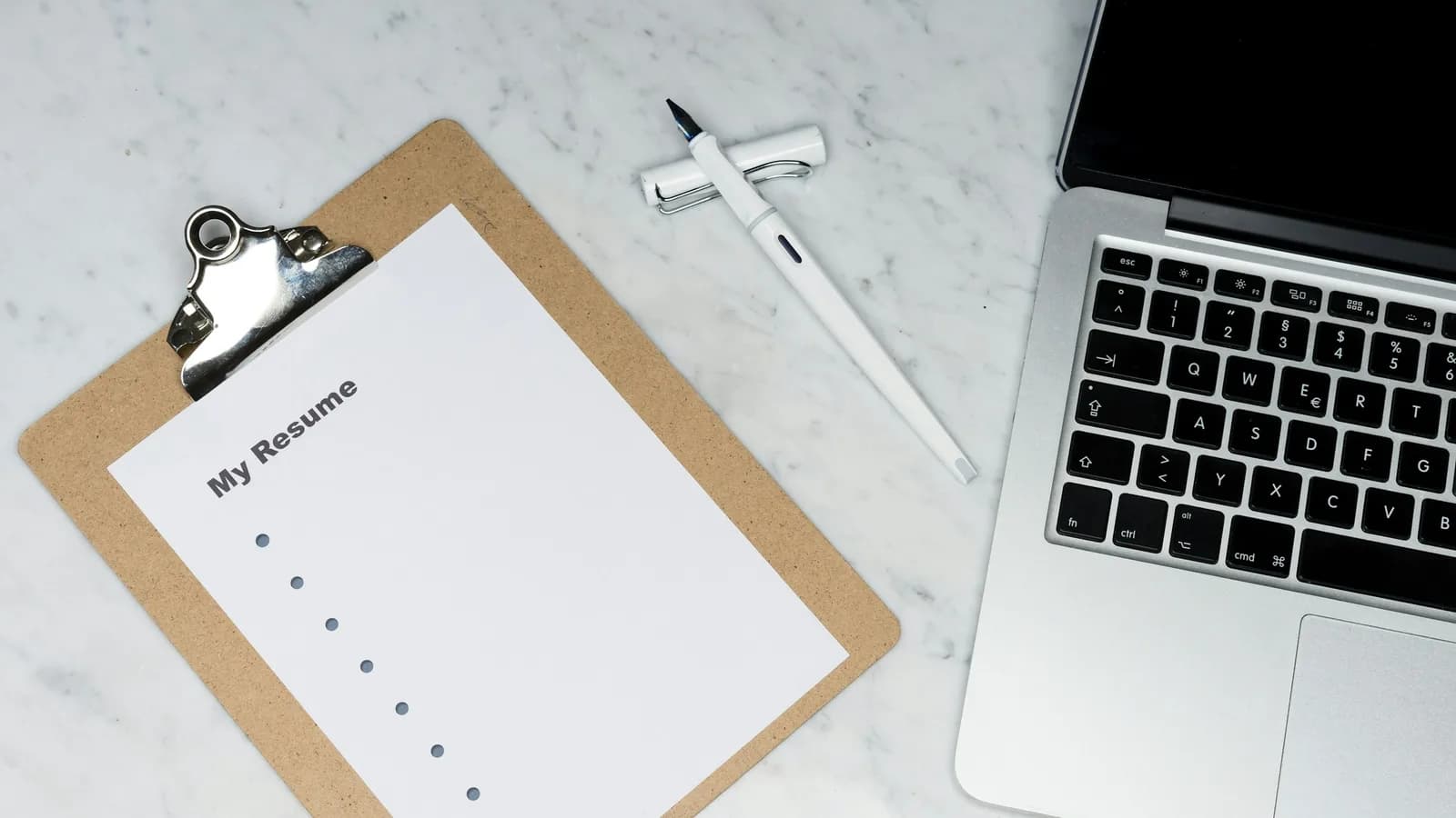 A plain resume on a clipboard next to a laptop, on a marble desk