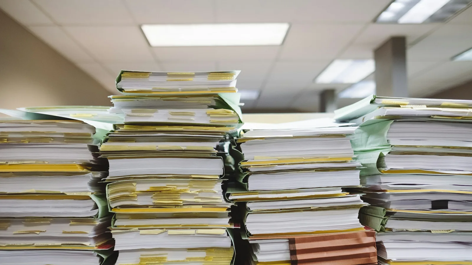 Tall stacks of paper files piled on an office desk