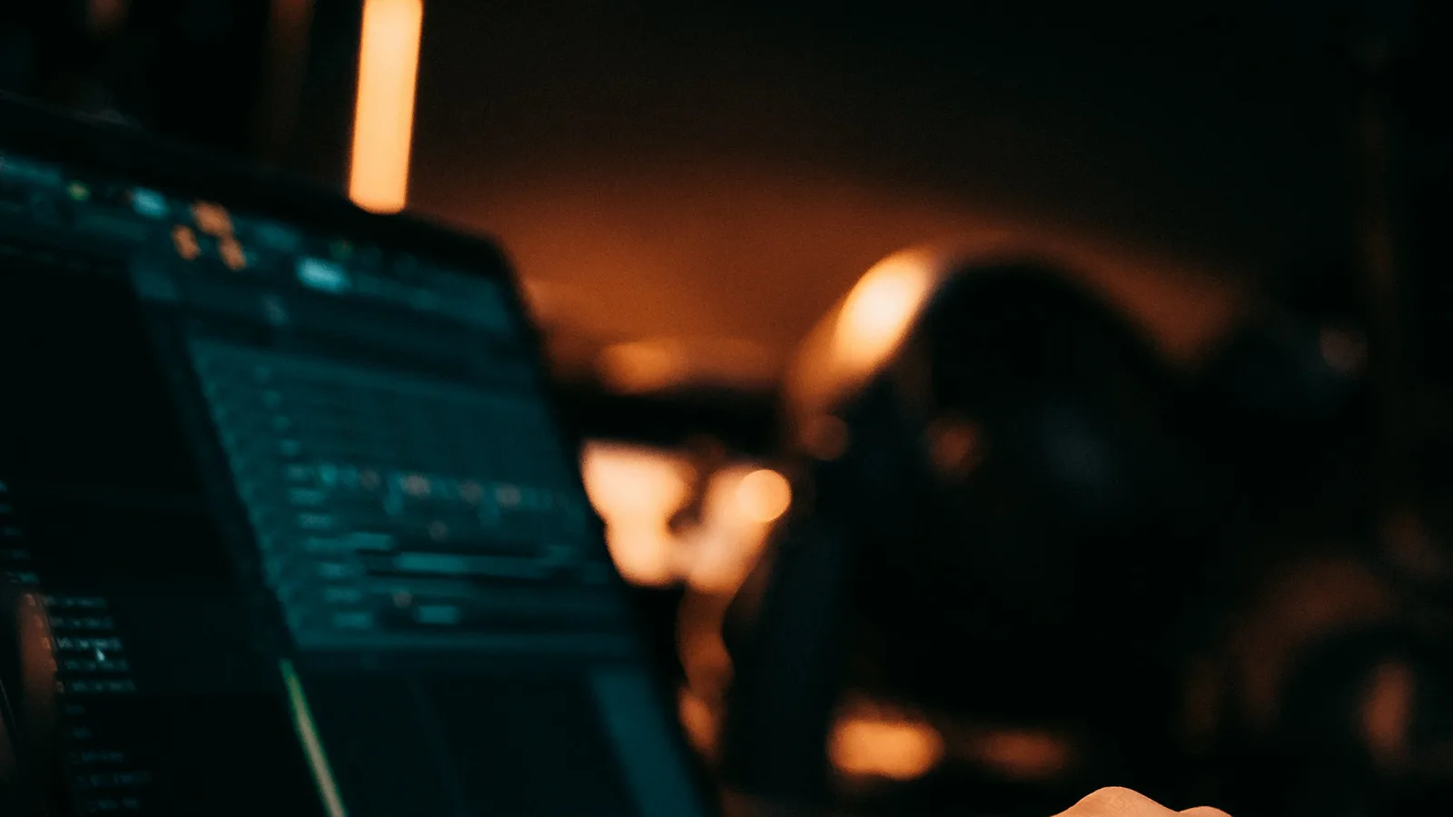 A hand typing on a laptop keyboard lit by a warm desk lamp at night